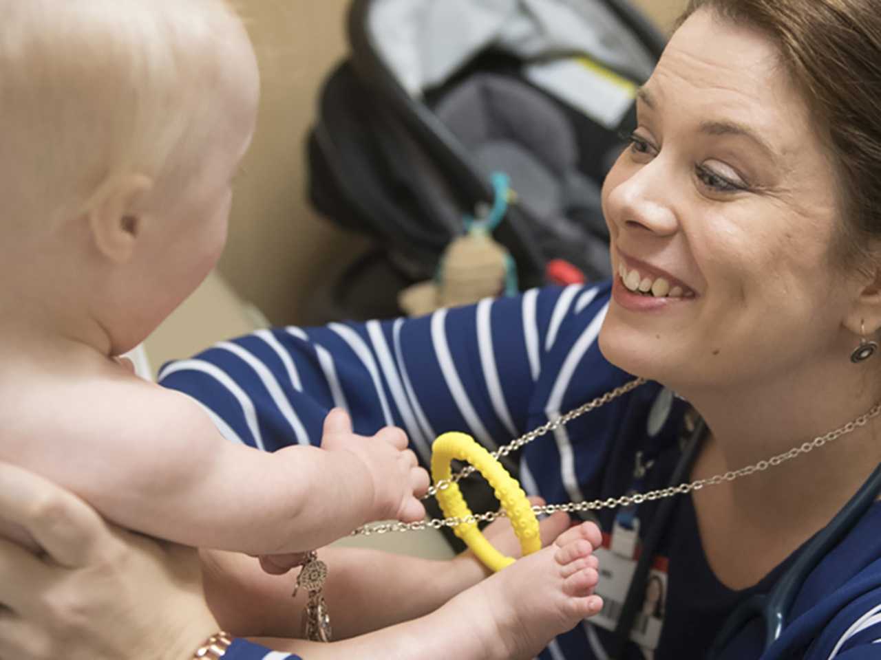 Woman holding baby who's playing with her necklace.