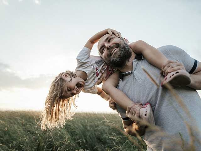 Father carrying daughter on his shoulders in a field and smiling