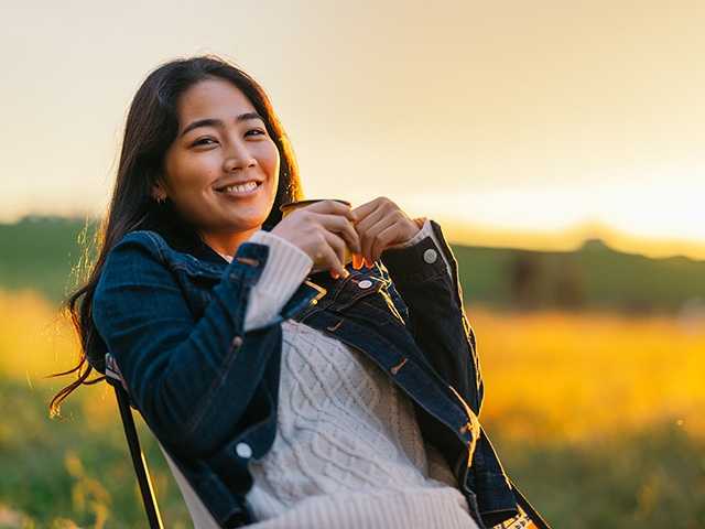 woman sitting, at sunset, with a mug, and smiling