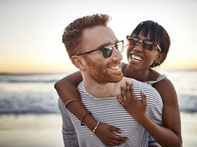 Man carrying woman on his back at the beach.