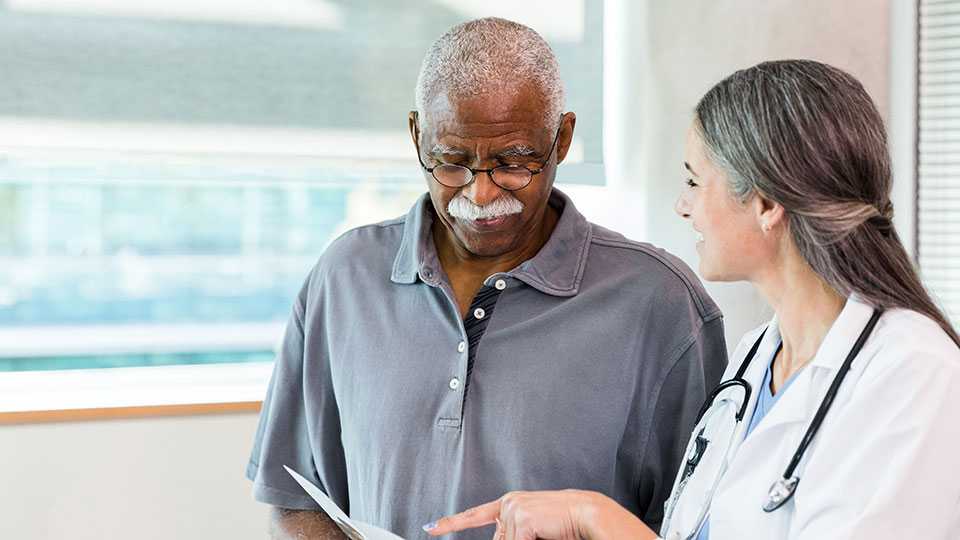 female doctor in lab coat standing next to male patient, pointing at paperwork